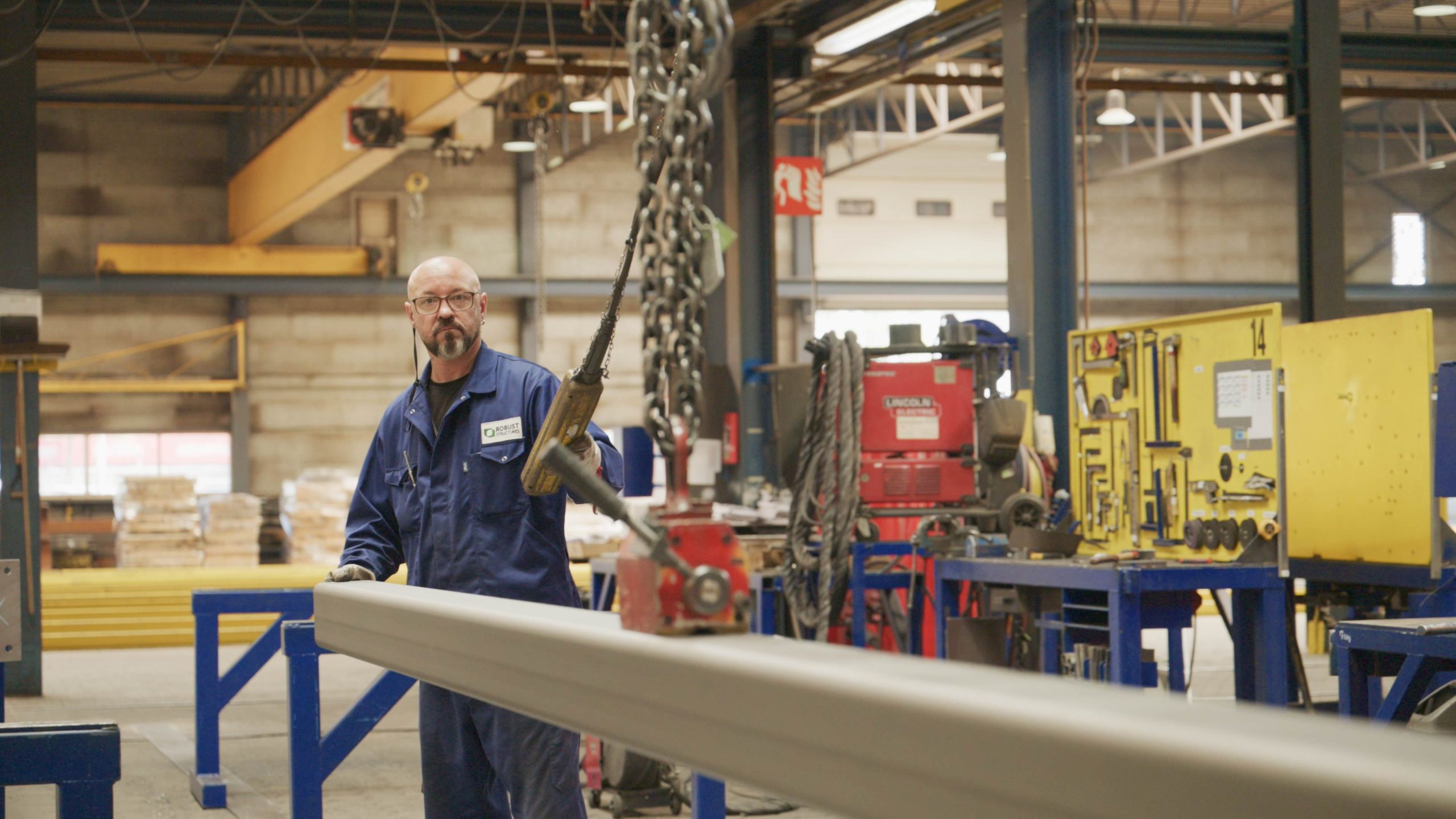 Monteur in werkplaats verplaatst metalen balk met een hijsinstallatie.